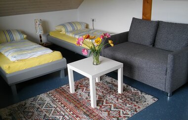 In einem Gästezimmer gibt es zwei Betten, ein Sofa und ein Beistelltisch. | © Touristikgemeinschaft Hohenlohe e. V. | Ferienwohnung / Gästehaus Heßlinger