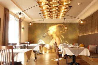 Frühstücksraum mit goldenem Bild von einer Frau im Hintergrund. Rechts gibt es eine Sitzbank mit Kissen und links stehen die Tische am Fenster. | © Neckar-Zaber-Tourismus e.V.