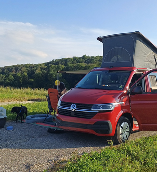 Ein roter VW-Bus mit Faltdach auf dem Platz mit einem Hund und einer Hundebox | © Touristikgemeinschaft Hohenlohe e. V. | Green Camp Schleierhof