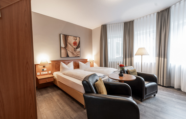 Hotelzimmer mit Doppelbett, zwei schwarzen Ledersesseln, einem runden Holztisch und einem Bild einer Frau mit rotem Lippenstift an der Wand | © Hotel Alexa