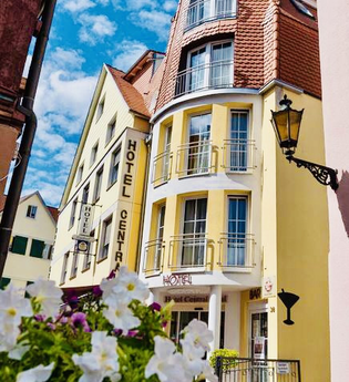 Gelbes Hotelgebäude mit roten Dachziegeln und Balkonen, daneben ein weiteres Hotel mit Schild 'Hotel Central', blauer Himmel mit Wolken, weiße Blumen im Vordergrund | © Hotel Central