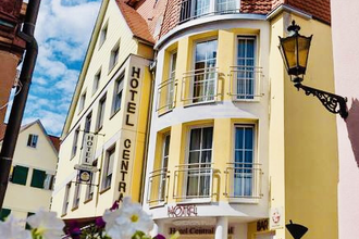 Gelbes Hotelgebäude mit roten Dachziegeln und Balkonen, daneben ein weiteres Hotel mit Schild 'Hotel Central', blauer Himmel mit Wolken, weiße Blumen im Vordergrund | © Hotel Central