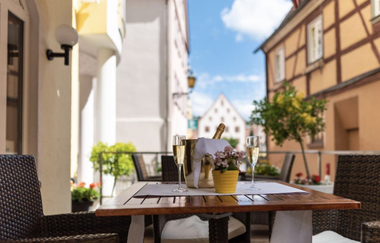 Holztisch mit zwei Sektgläsern, einem Eiskübel mit Sektflasche und einer kleinen gelben Blumentopf mit rosa Blumen auf einer Terrasse in einer Altstadt | © Hotel Central