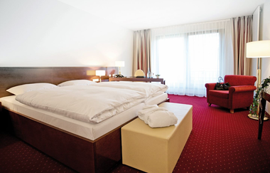 Ein Doppelzimmer mit Bett und Sessel | © Touristikgemeinschaft Hohenlohe e. V.