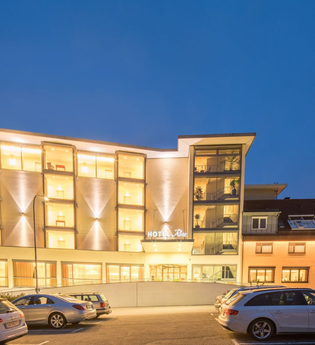 Das Hotel ist nachts hell beleuchtet, davor ist ein Parkplatz für Pkw | © Touristikgemeinschaft Hohenlohe e. V.