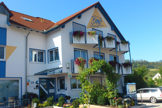 Gästehaus Birgit mit blumengeschmückten Balkonen, grünem Pflanzenbogen am Eingang und mehreren geparkten Autos vor dem Haus | © Gästehaus Birgit