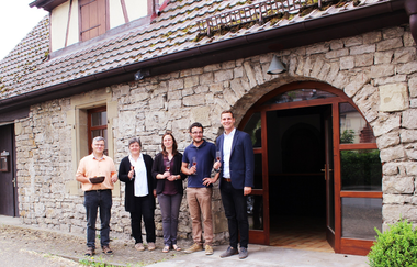 Drei Männer und zwei Frauen stehen mit einem Glas Wein vor dem Eingang vom Weingut, Besenwirtschaft und Kelterhotel | © Touristikgemeinschaft Hohenlohe e. V.  | Rebenhof Fröscher