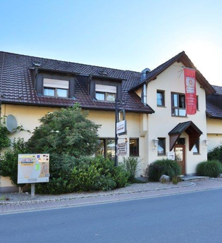 Außenansicht des Landgasthofs Taubertal mit gelbem Gebäude, braunem Dach und Schildern am Eingang | © Landgasthof Taubertal