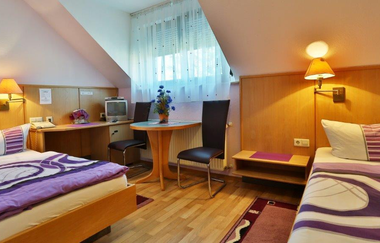 Zweibettzimmer im Landgasthof Taubertal mit zwei Einzelbetten, lila Bettwäsche, kleinem Tisch mit zwei Stühlen und Fernseher am Fenster | © Landgasthof Taubertal