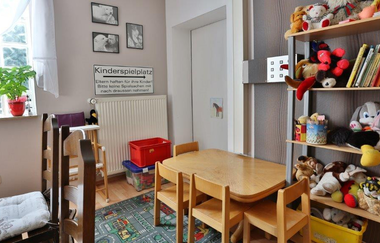 Kinderspielecke mit kleinem Holztisch und vier Stühlen, Regal mit Kuscheltieren und Büchern, Fenster mit Pflanzen, Schild 'Kinderspielplatz' an der Wand | © Landgasthof Taubertal