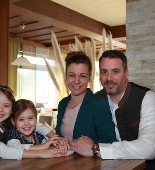 Die Eltern und zwei Mädchen sitzen zusammen am Tisch und lächeln in die Kamera | © Touristikgemeinschaft Hohenlohe e. V. | Landhotel Küffner