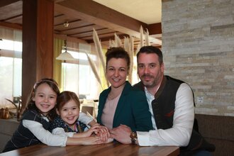 Die Eltern und zwei Mädchen sitzen zusammen am Tisch und lächeln in die Kamera | © Touristikgemeinschaft Hohenlohe e. V. | Landhotel Küffner