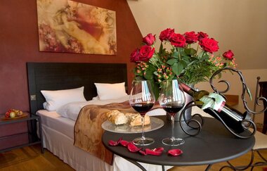 Blick in die Juniorsuite "Wein, Weib & Gesang" mit Bett, Tisch, Wein und einem Strauß roter Rosen im Hotel Laurentius in Weikersheim. | © Unbekannt