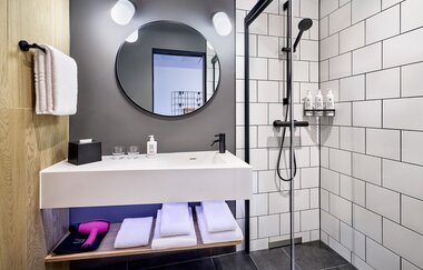 Modernes Bad mit weißen Kacheln, begehbarer Dusche und einem weißen Waschtisch | © Touristikgemeinschaft Hohenlohe e. V. | Moxy Kupferzell Hohenlohe