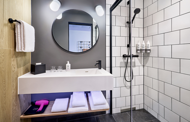 Modernes Bad mit weißen Kacheln, begehbarer Dusche und einem weißen Waschtisch | © Touristikgemeinschaft Hohenlohe e. V. | Moxy Kupferzell Hohenlohe