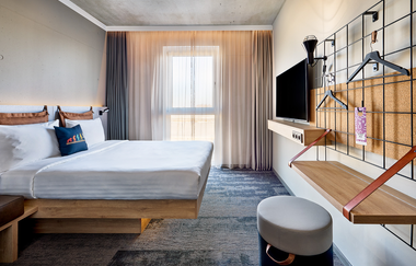 Im Zimmer steht ein Doppelbett, ein TV-Gerät und ein klappbares Board | © Touristikgemeinschaft Hohenlohe e. V. | Nemis Hotel Hohenlohe GmbH