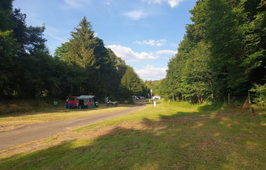 Auf dem Bild ist der Naturcampingplatz in Bad Mergentheim zu sehen, ein Weg mit Wiesenflächen rechts und links und  großen Bäume im Hintergrund. Ein Stellplatz ist mit Zelt/Auto und Motorrad belegt. Ein sonniger Tag mit blauem Himmel und weißen Wolken.. | © Unbekannt