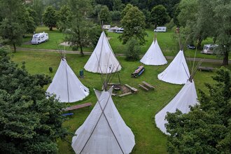 Blick von oben auf eine Wiese mit 6 Tipis die in einem Kreis stehen. In der Mitte ist eine Feuerstelle mit Bänken. Neckargerach im Odenwald. | © ODENWALD river camp