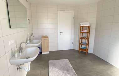 Großes Badezimmmer mit zwei Waschbecken und einem großen Spiegel. Die Wände sind weiß und es gibt einen kleinen hölzernen Schrank und ein Holzregal | © Neckar-Zaber-Tourismus e.V.