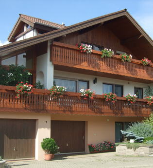 Das Gebäude hat zwei Holzbalkone, an denen Blumen blühen | © Touristikgemeinschaft Hohenlohe e. V. | Familie Beez