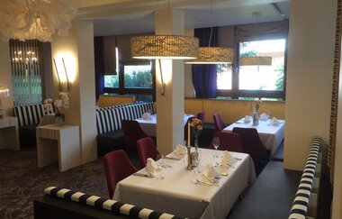 Innenraum des Restaurants Bundschu mit gedeckten Tischen, gestreiften Sitzbänken und modernen Hängeleuchten | © Ringhotel Bundschu