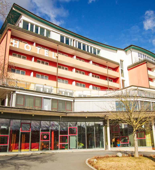 Mehrstöckiges Hotelgebäude mit roten Balkonen und großen Glasfenstern, darunter ein Bistro-Eingang, unter blauem Himmel | © Savoy Hotel