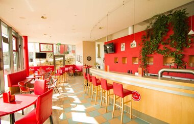 Helle Bar mit roten Stühlen und Tischen, langer Holztheke, roten Wandnischen und grünen Pflanzen an der Wand | © Savoy Hotel