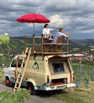 Der Trapperbus steht in den Weinbergen. Zwei Personen sitzen auf der Dachterrasse.