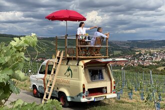 Der Trapperbus steht in den Weinbergen. Zwei Personen sitzen auf der Dachterrasse.