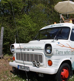 Ein umgebauter Bus zum übernachten. Eine Leiter führt auf der rechten Seite auf das Dach, wo sich eine kleine Terrasse mit Stühlen und Sonnenschirm befindet. | © Tourist-Information