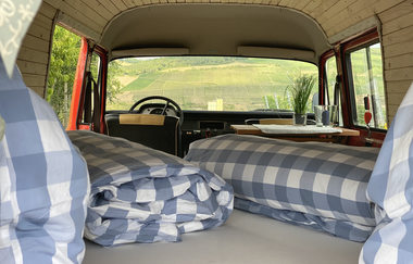 Kissen und Bettdecken im Innenraum des Busses. Aus dem Fenster sieht man die Weinberge. | © Jakobshof Lehr