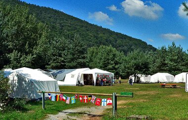 Blick auf den Jugendzeltplatz auf dem Seecamping-Platz in Freudenberg. Im Vordergrund ist eine Schranke mit vielen verschiedenen Fahnen-Wimpeln zu sehen. | © Liebliches Taubertal