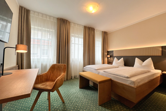 Ein Doppelzimmer im Hotel mit grünem Teppichboden. Ein Tisch mit einem Sessel stehen vor dem Bett. | © Stadthotel Münze