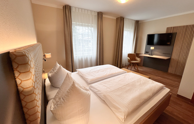 Ein Doppelzimmer im Hotel mit Holzboden. Fernseher, Tisch und Sessel stehen im Hintergrund. | © Stadthotel Münze