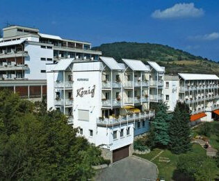 Außenansicht des Vitalhotels König, ein mehrstöckiges weißes Hotelgebäude umgeben von Bäumen und Hügeln unter blauem Himmel | © Vitalhotel König