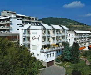 Außenansicht des Vitalhotels König, ein mehrstöckiges weißes Hotelgebäude umgeben von Bäumen und Hügeln unter blauem Himmel | © Vitalhotel König