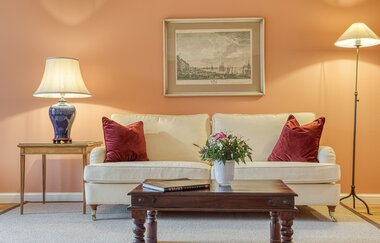 Vor der eleganten Couch in weiß steht ein antiker Tisch | © Touristikgemeinschaft Hohenlohe e. V. | Wald & Schlosshotel Friedrichsruhe