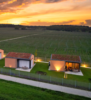 Vogelperspektive-Blick auf die vier Chalets und dahinter liegende Weinberge bei Sonnenuntergang | © Weingut Becker, Malsch