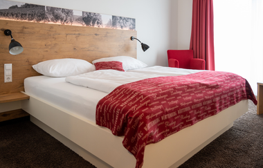 Modern eingerichtetes Hotelzimmer im Vinotel Schwab mit weiß-roter Bettwäsche, rotem Sessel und roten Vorhängen | © Touristikgemeinschaft Hohenlohe | Heinz J. Schwab