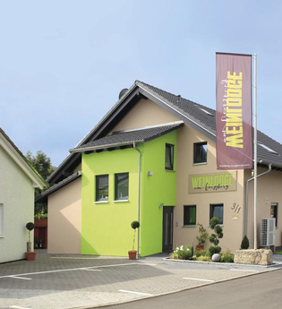 Gebäude von Außen zu sehen mit grünem und braunen Farben und einer großen Fahne im Vordergrund mit Weinlodge