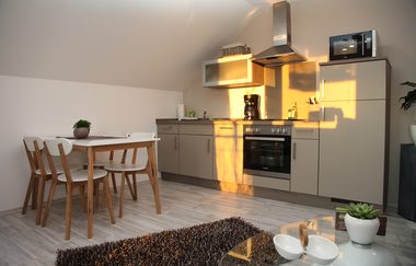 Ferienwohnung Küchenansicht mit Tisch, 4 Stühlen, Küchenzeile und im Vordergrund ein Glastisch und Teppich