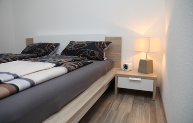 Schlafzimmer mit 1,40m Bett, Nachttisch mit Lampe und Wecker