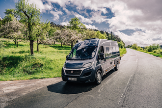 Dunkler Kastenwagen fährt auf einer Straße. Links vom Wohnmobil ist eine Streuobstwiese.| Odenwald | © Touristikgemeinschaft Odenwald e.V.