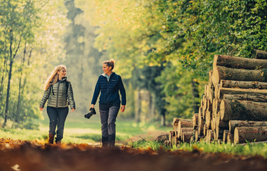 2 Personen laufen auf einem mit Blätter bedeckten Weg. Links und rechts vom Weg stehen Bäume. Zudem liegt auf der rechten Seite am Wegrand ein Haufen Baumstämme| Odenwald | © Touristikgemeinschaft Odenwald e.V.