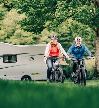 Zwei Radfahrer im Hintergrund ein weißes Wohnmobil und Bäume. Odenwald. | © Touristikgemeinschaft Odenwald e.V.