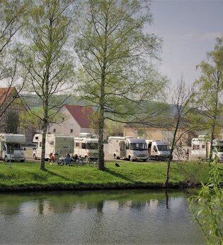 Blick auf den direkt an der Tauber gelegenen Wohnmobilstellplatz in Röttingen. Der Platz ist gut besucht. Im Hintergrund sind Häuser zu sehen. | © Tourist-Information Röttingen