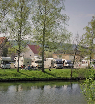 Blick auf den direkt an der Tauber gelegenen Wohnmobilstellplatz in Röttingen. Der Platz ist gut besucht. Im Hintergrund sind Häuser zu sehen. | © Tourist-Information Röttingen