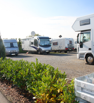 Ein geschotterter Platz mit vielen weißen Wohnmobilen. Im Vordergrund wird der Platz durch eine grüne Hecke begrenzt. Walldürn im Odenwald. | © Goldschmitt techmobil GmbH