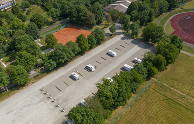 Luftaufnahme vom Wohnmobilstellplatz mit direktem Blick nach unten. Wohnmobile stehen auf dem Stellplatz.
