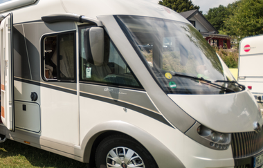 Frontansicht eines geparkten, modernen Wohnmobils mit großen Fenstern auf einer grünen Wiese. | © Dominik Ketz